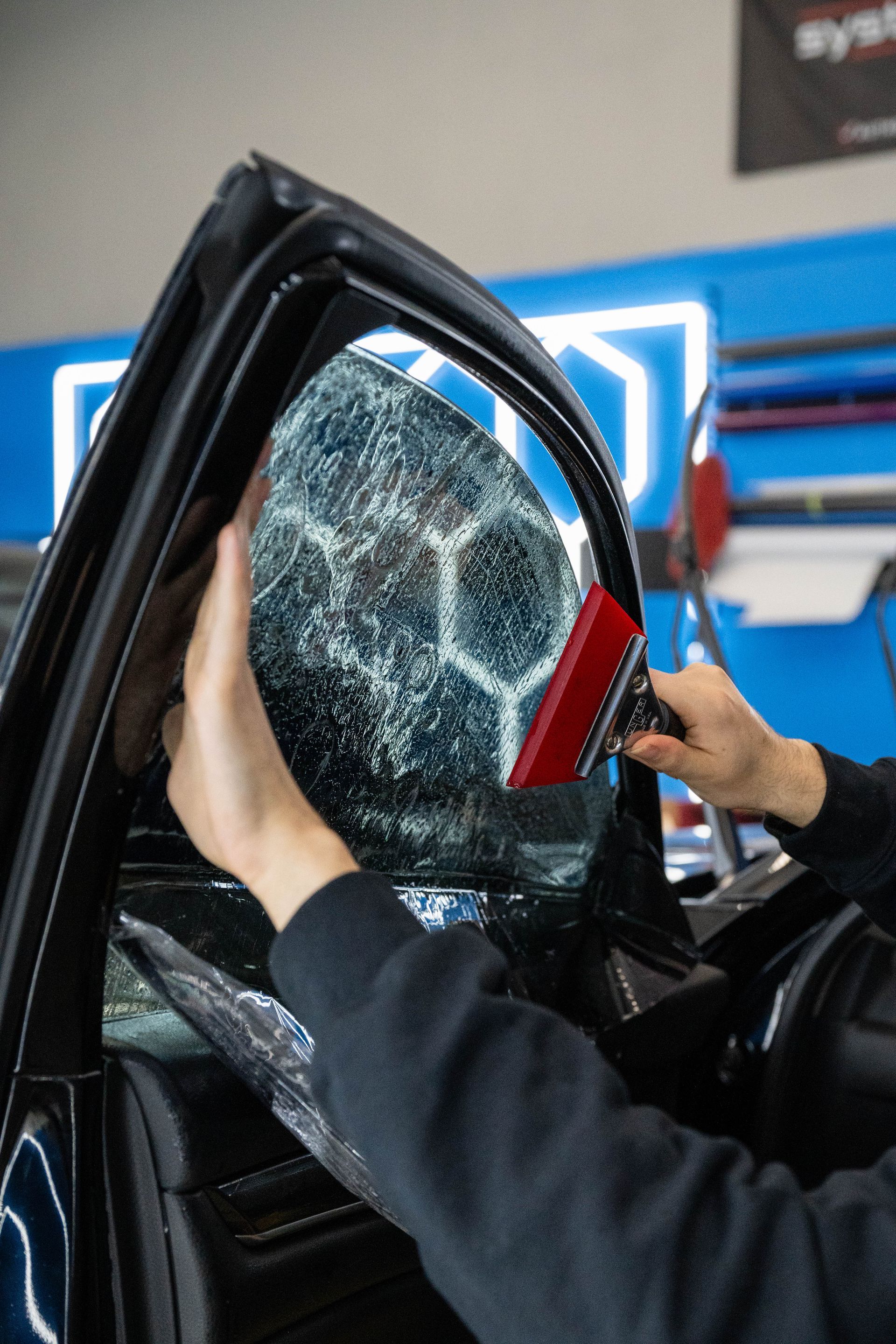 Person applying window tint to a car window with a squeegee.