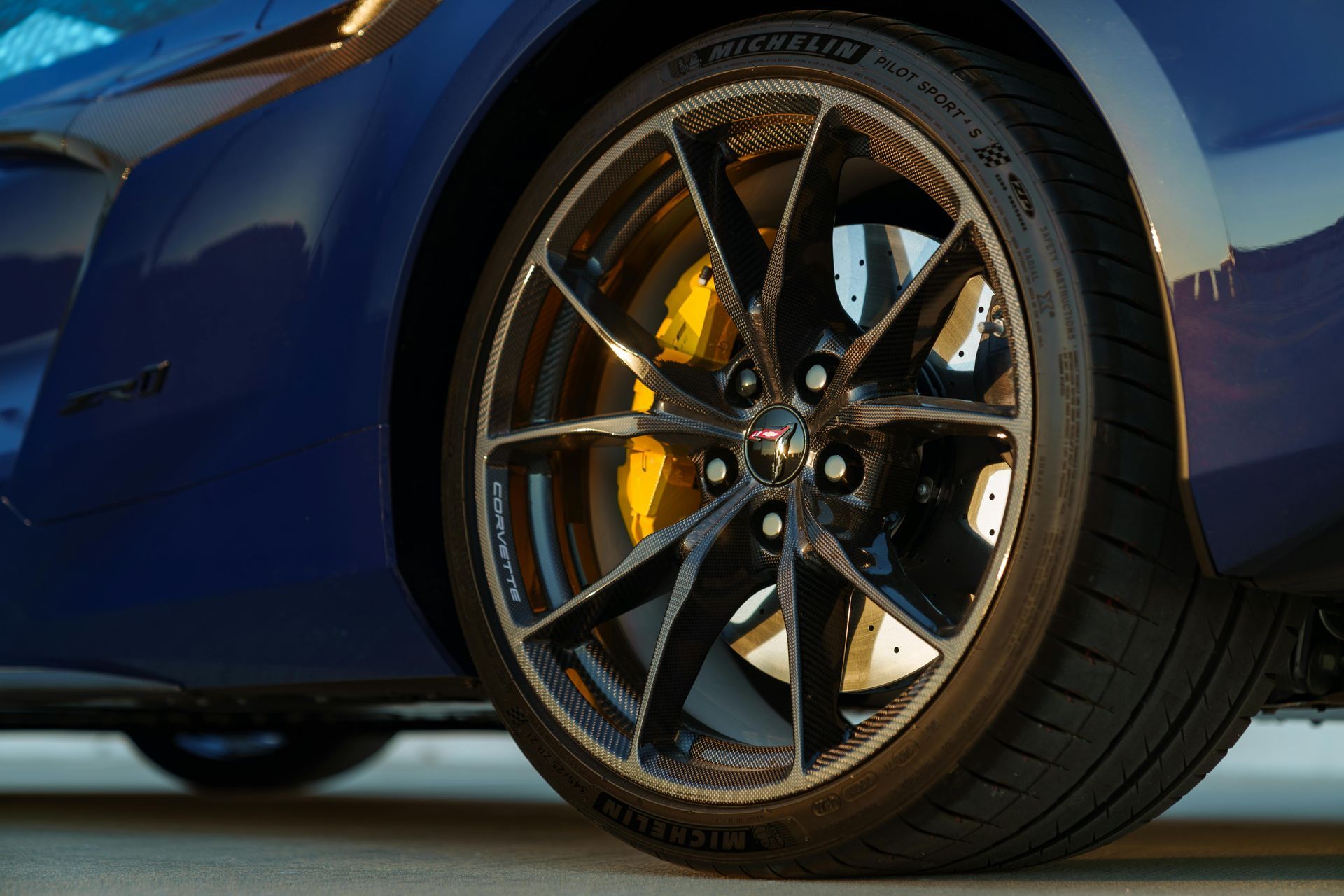 Blue sports car wheel with black rim, yellow brake caliper, and Michelin tire.