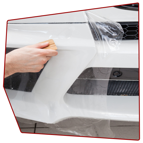 Person applying protective film to a white car bumper with a squeegee. Person applying protective film to a white car bumper with a squeegee.
