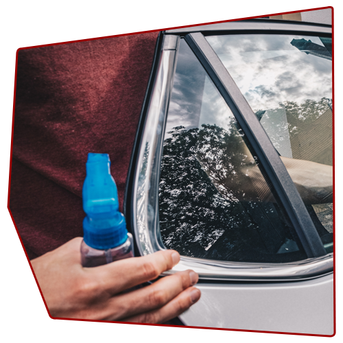 Person holding a blue bottled drink next to a car window reflecting trees and sky.