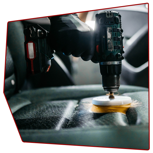 Person using a drill with a scrubbing brush on a car seat. Person using a drill with a scrubbing brush on a car seat.