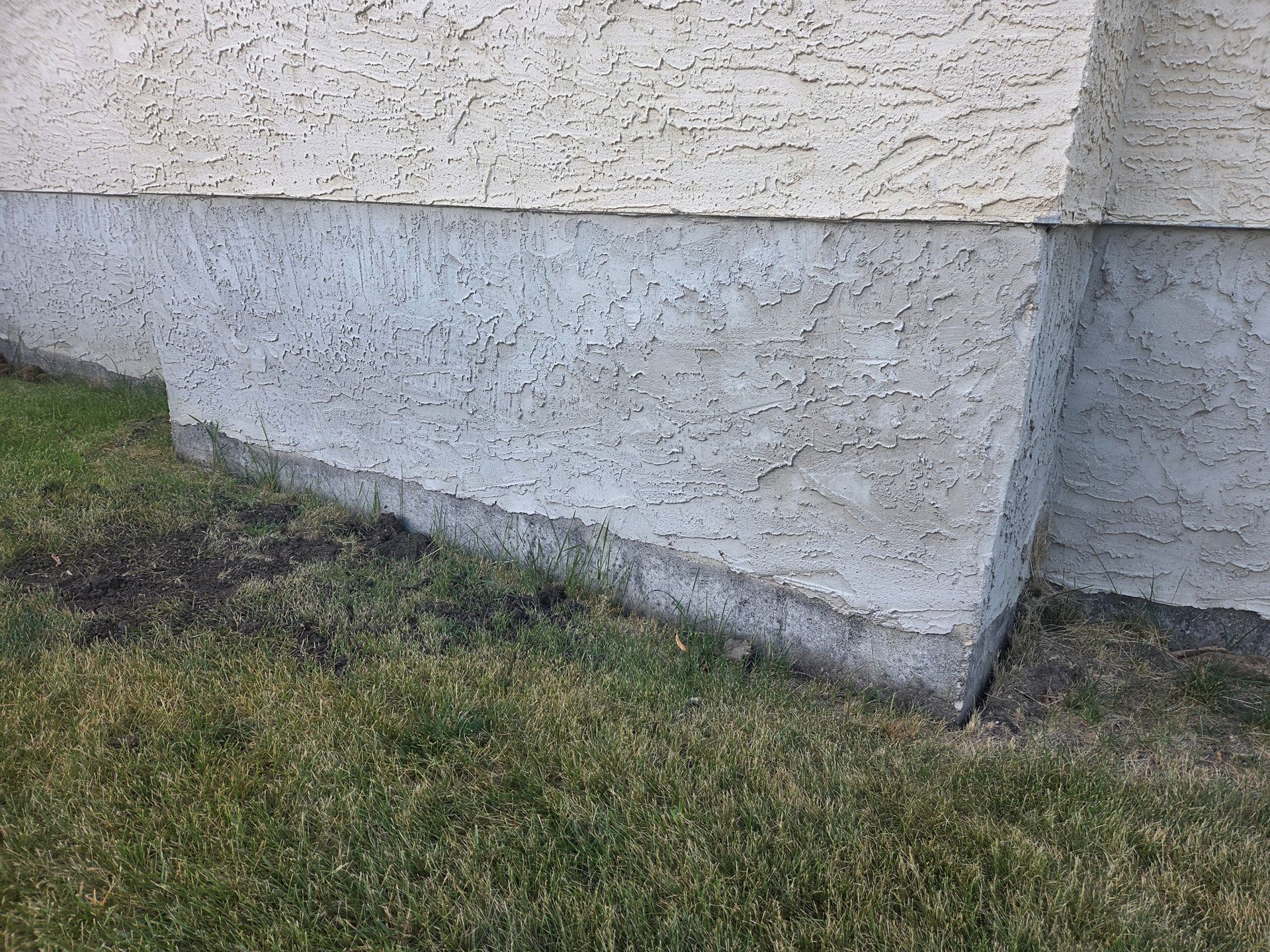 Exterior stucco wall corner above a patchy grass lawn