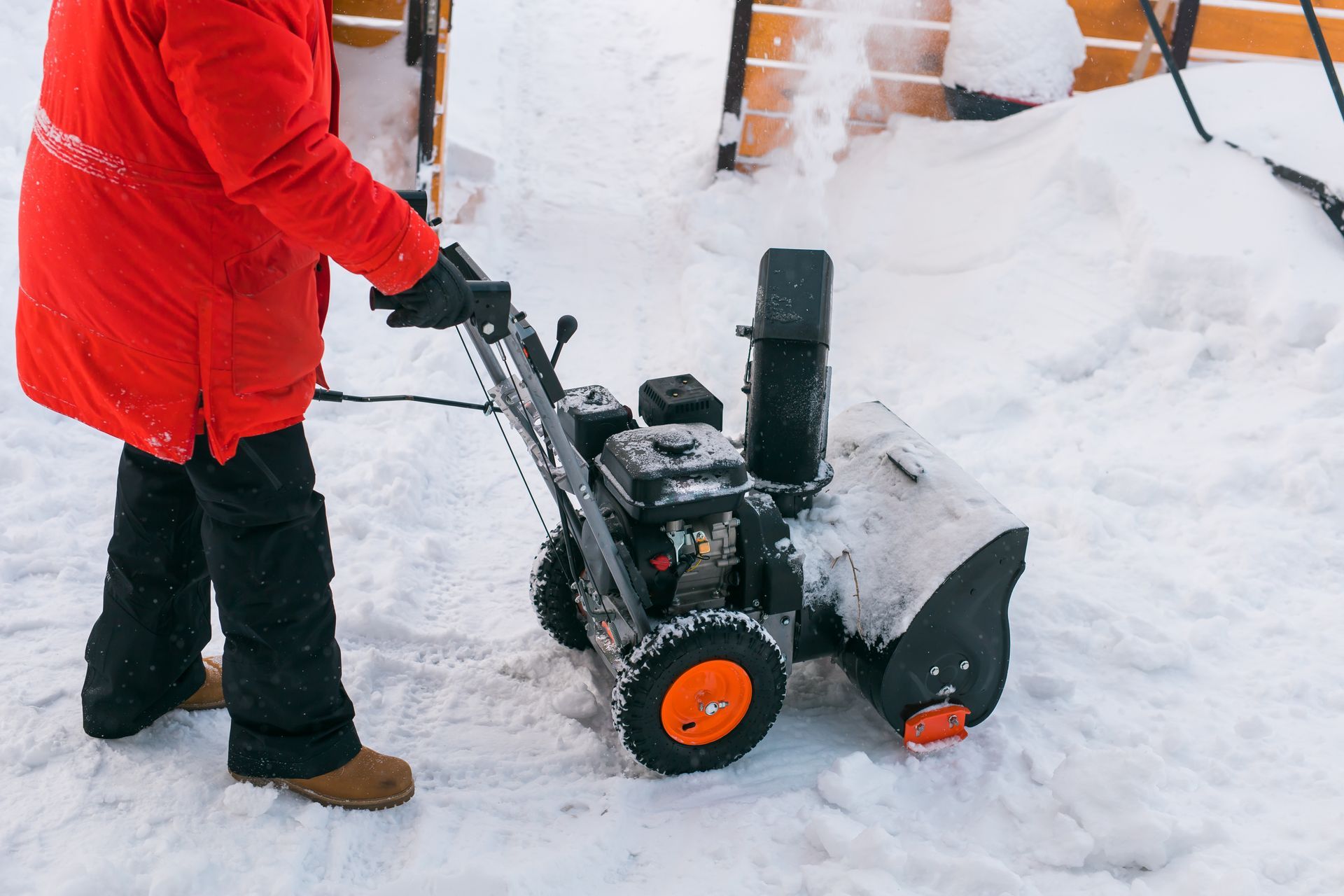 Person in red coat clearing snow with a snowblower outside a house
