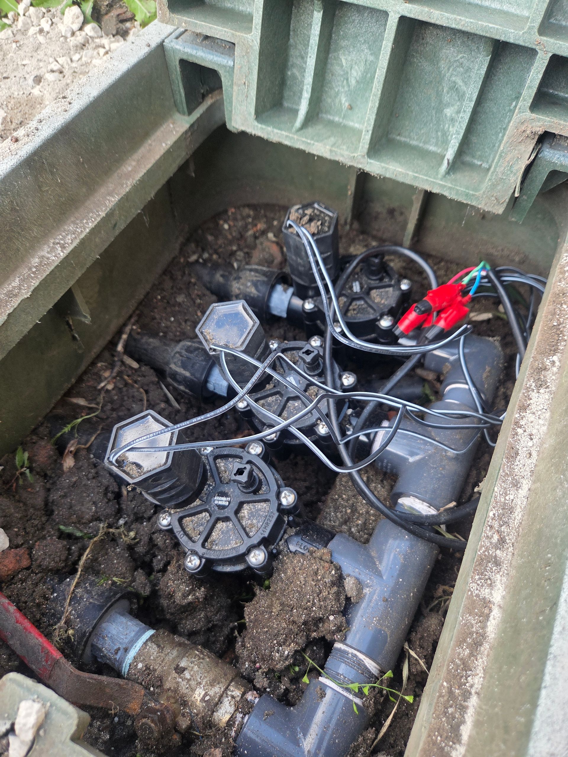Open valve box with water shutoff valves, pipes, and a red tool inside underground chamber