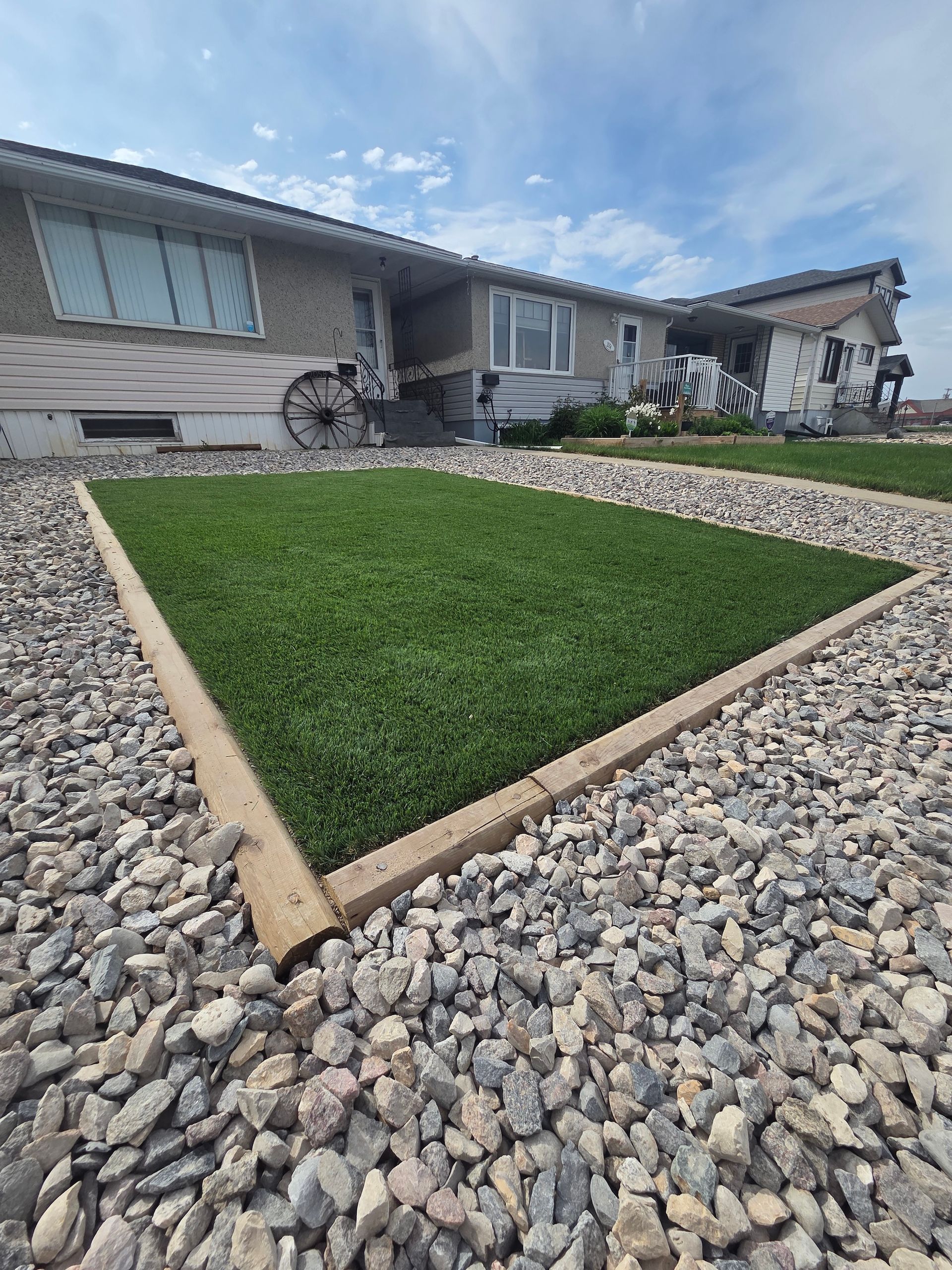 Landscaped yard with a triangular green lawn bordered by rocks in front of a suburban house