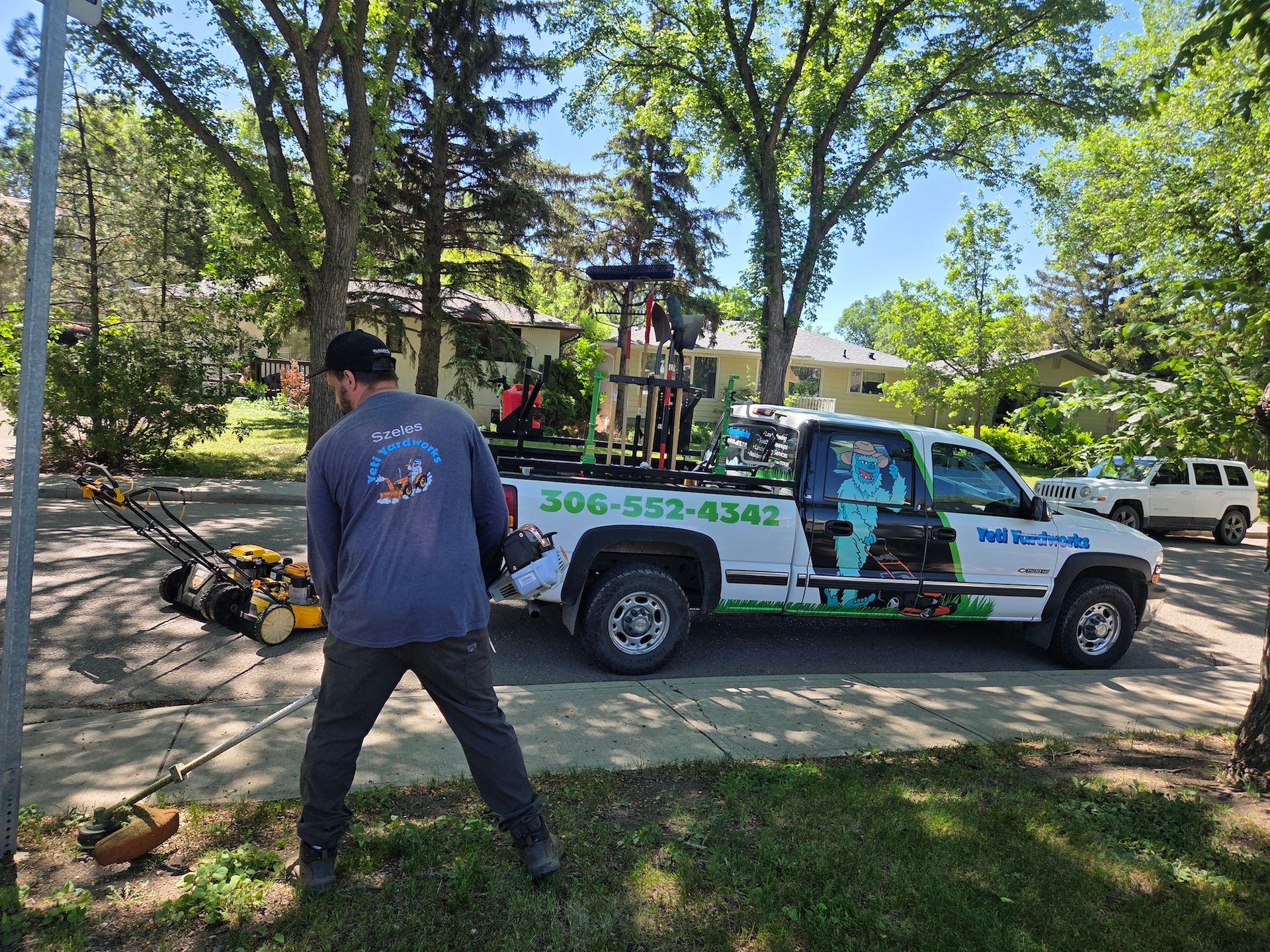 Worker in blue shirt on a residential street beside a white utility truck and fallen tree branches