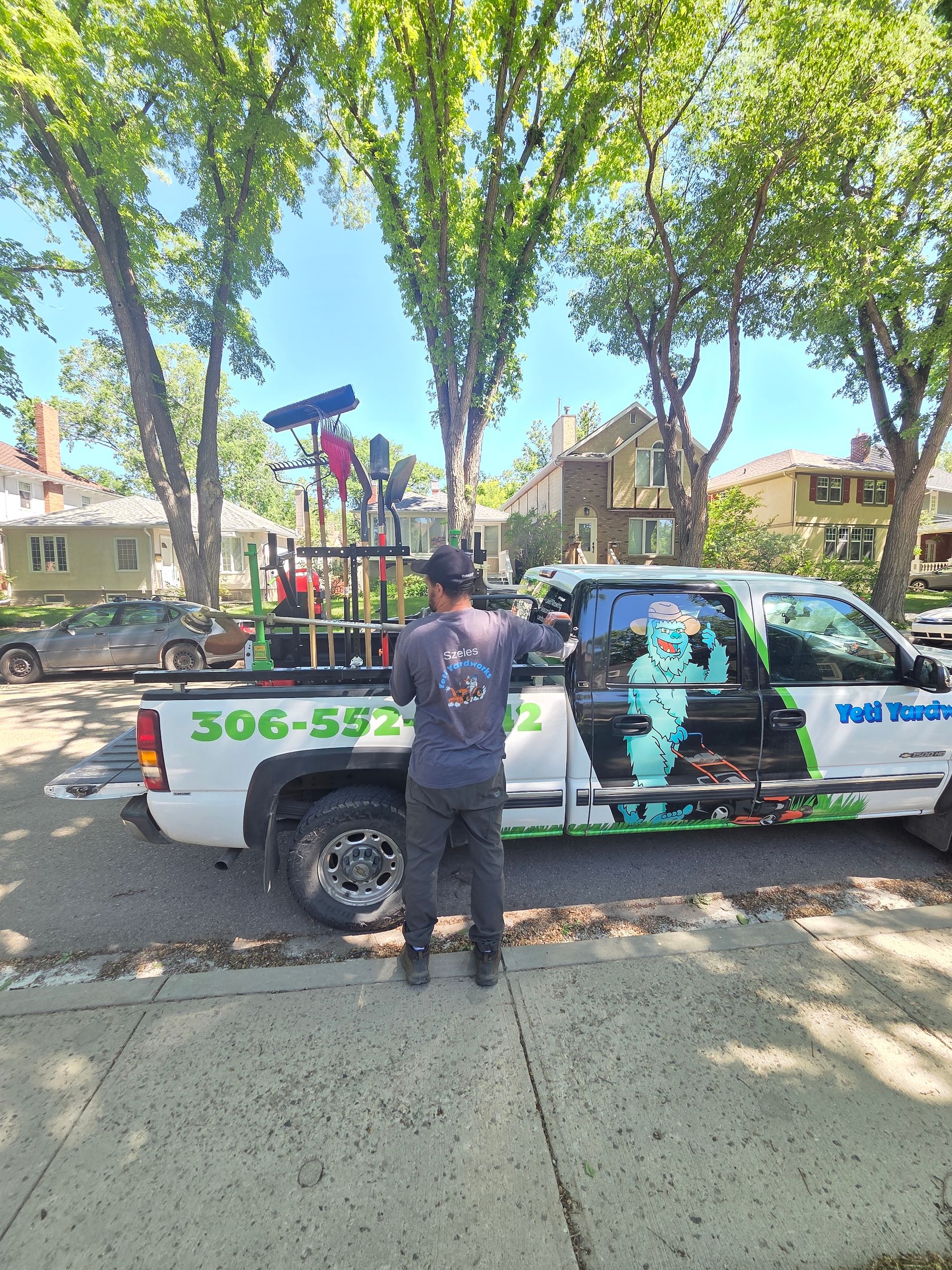 Man beside a colorful truck parked on a tree-lined street, with large green phone number on the side.