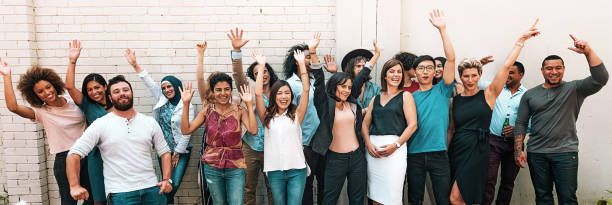 Group of people standing together, smiling and raising their hands in front of a brick wall