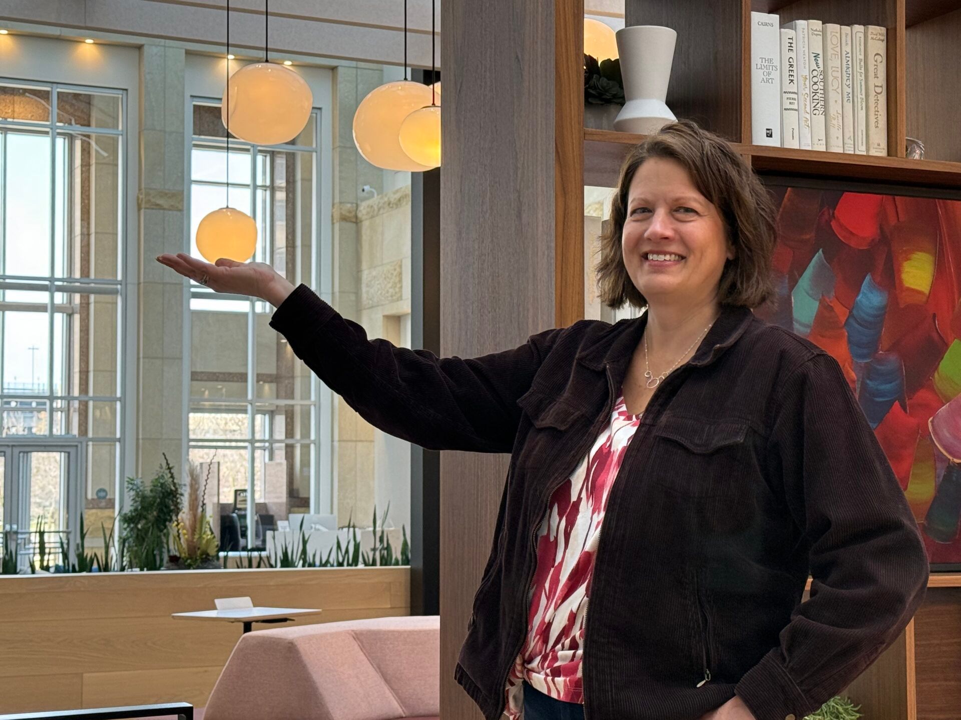 Woman smiling and gesturing toward hanging lights in a modern office lounge