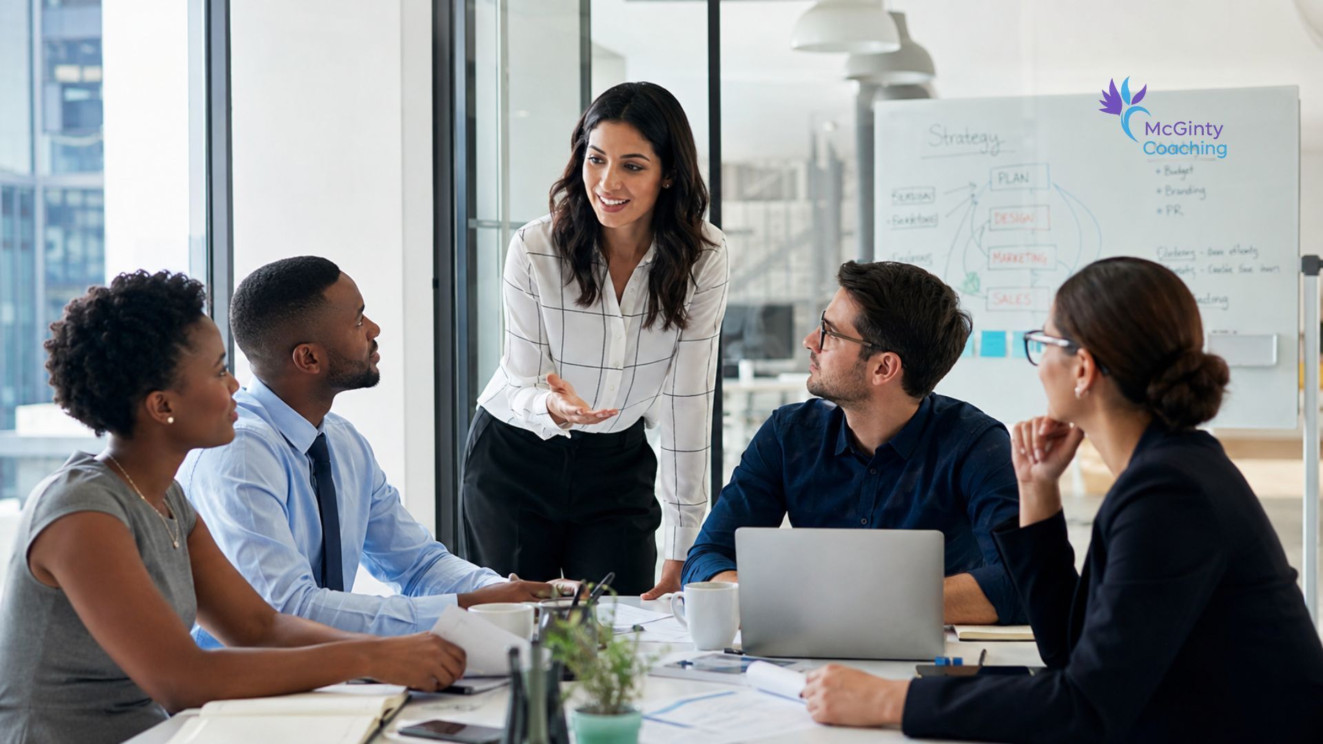 Team meeting in a bright office, with a woman presenting to four colleagues around a conference table.