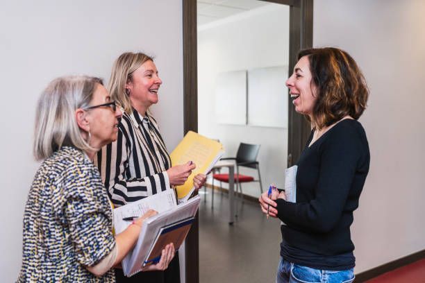 Three people chatting in a hallway, one holding a yellow folder and another holding a notebook.