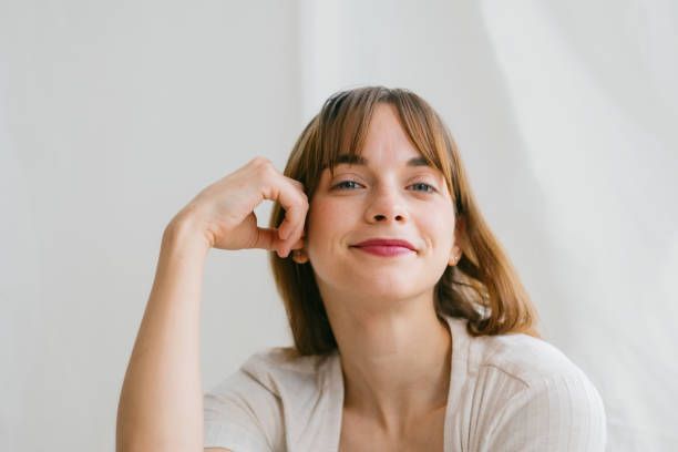 Woman with a slight smile, resting her head on her hand; wearing a light colored shirt.