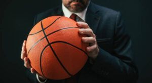 Man in suit holding a basketball. Dark background.