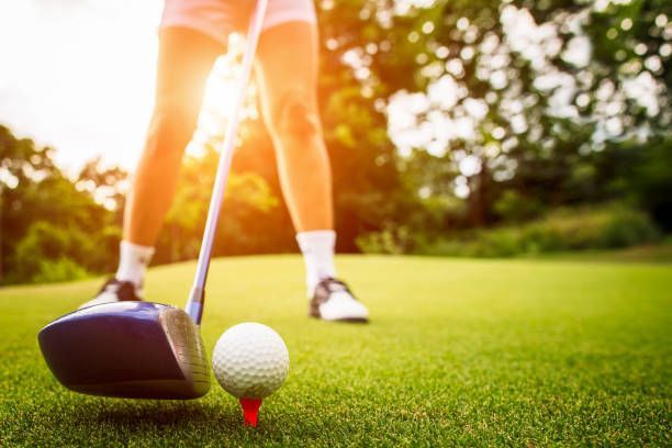 A golfer prepares to hit a ball resting on a red tee, with sunlight glowing in the background on a green golf course.