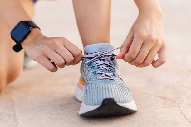 Hands tying the laces of a blue running shoe on a pavement.