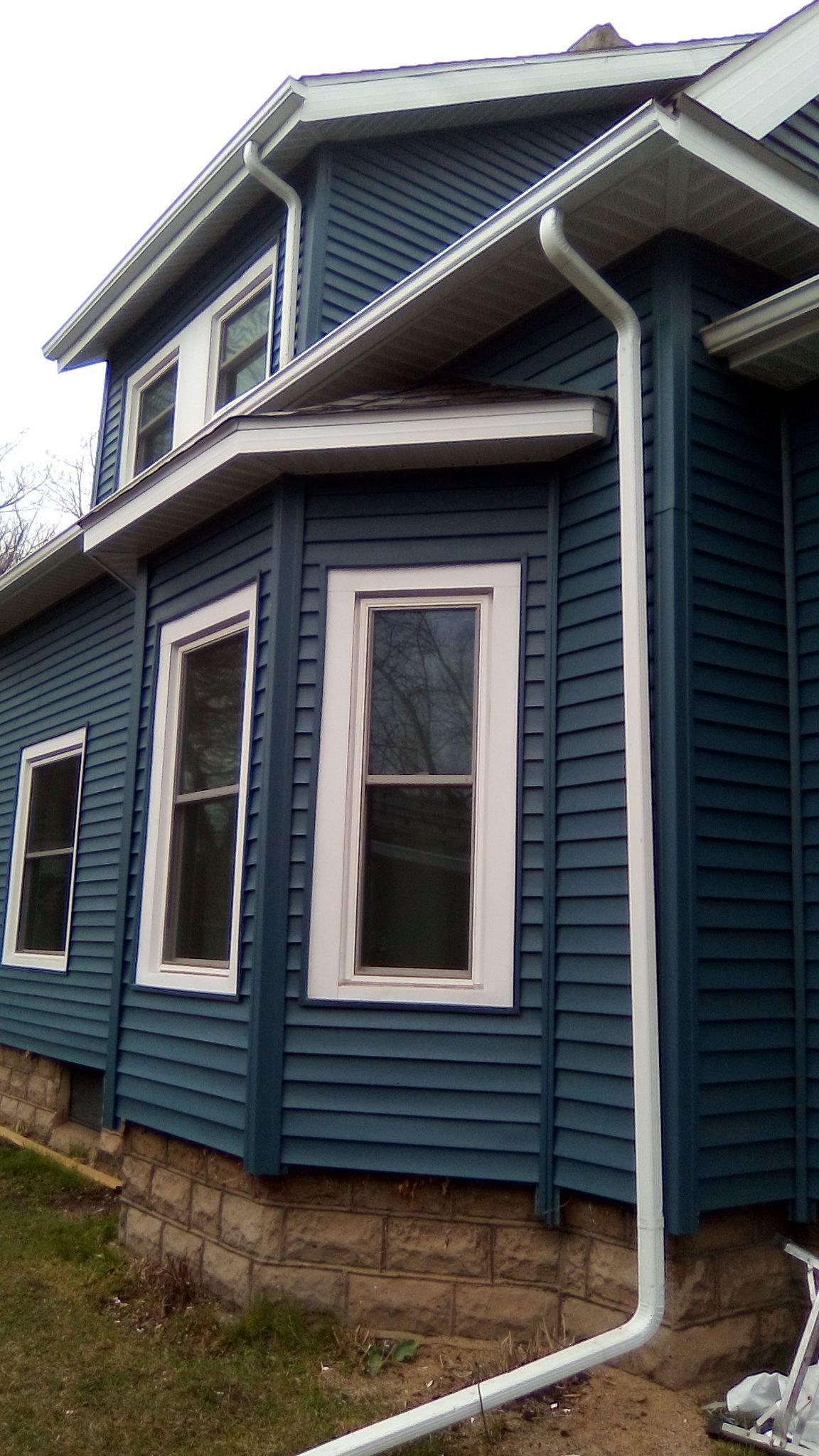 Blue house exterior with white-trimmed windows and roof overhang, viewed from the side.