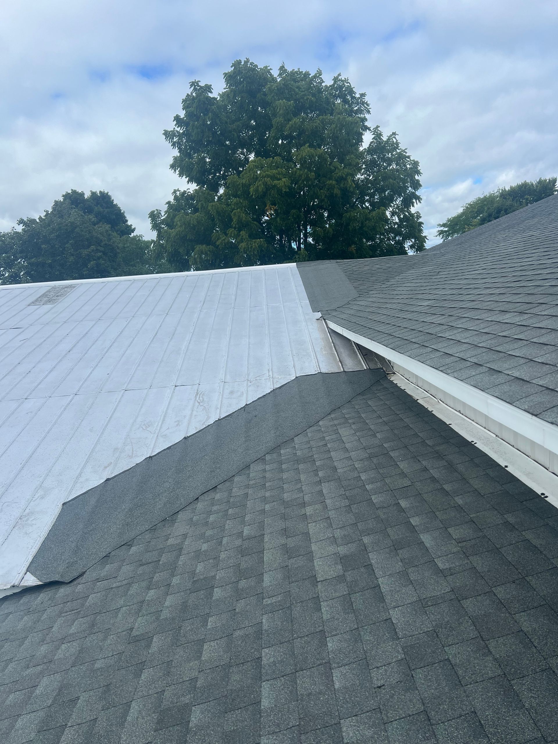 Roof repair with gray shingles and a white underlayment exposed under a cloudy sky