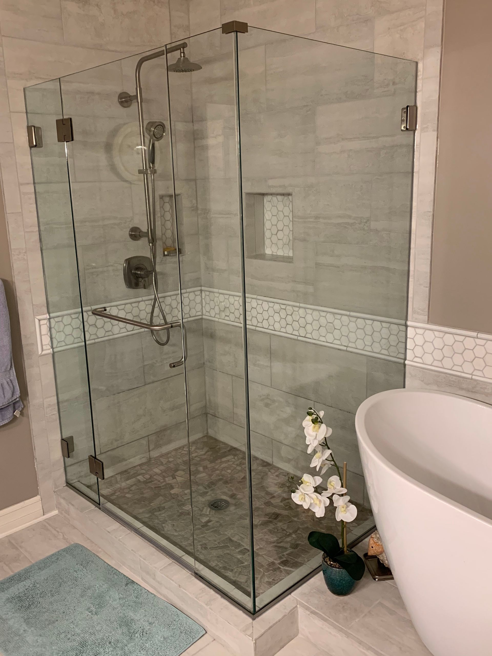 Glass shower enclosure in a tiled bathroom with a showerhead and a small potted orchid nearby