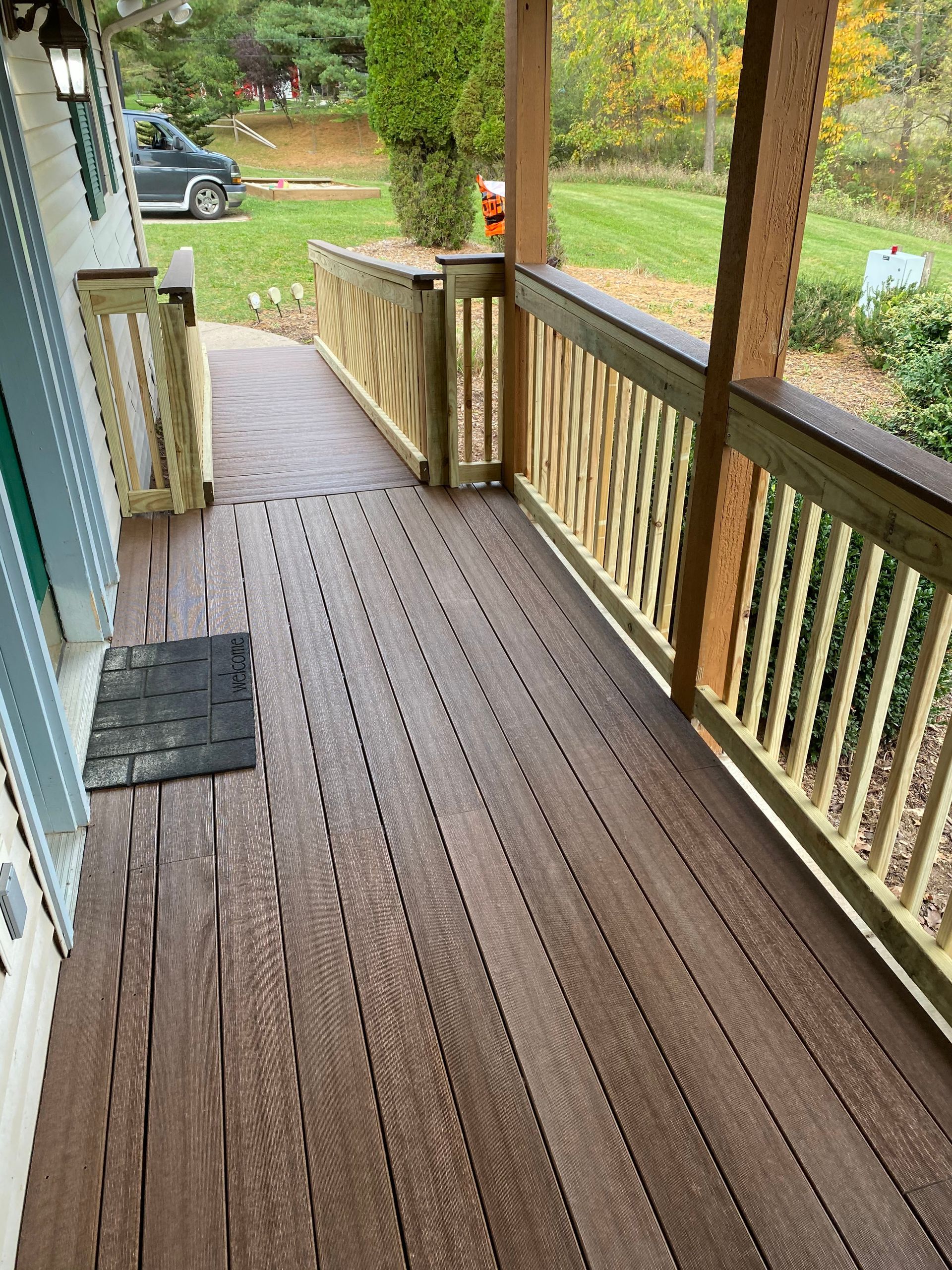 Wooden porch with railings and posts, leading to a yard with trees and a parked truck.