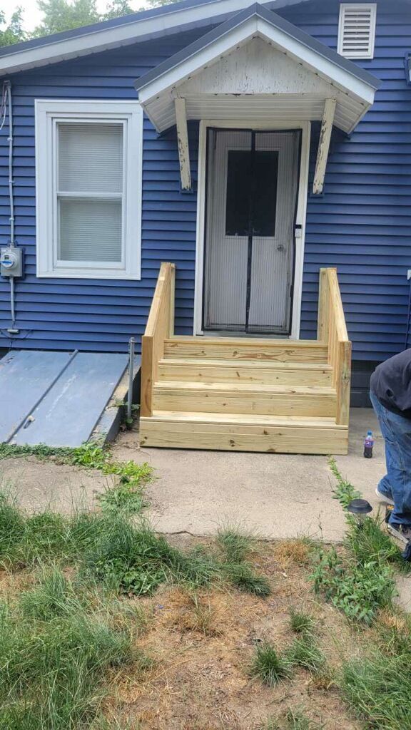 Wooden steps and railing leading to a white front door on a blue house exterior.