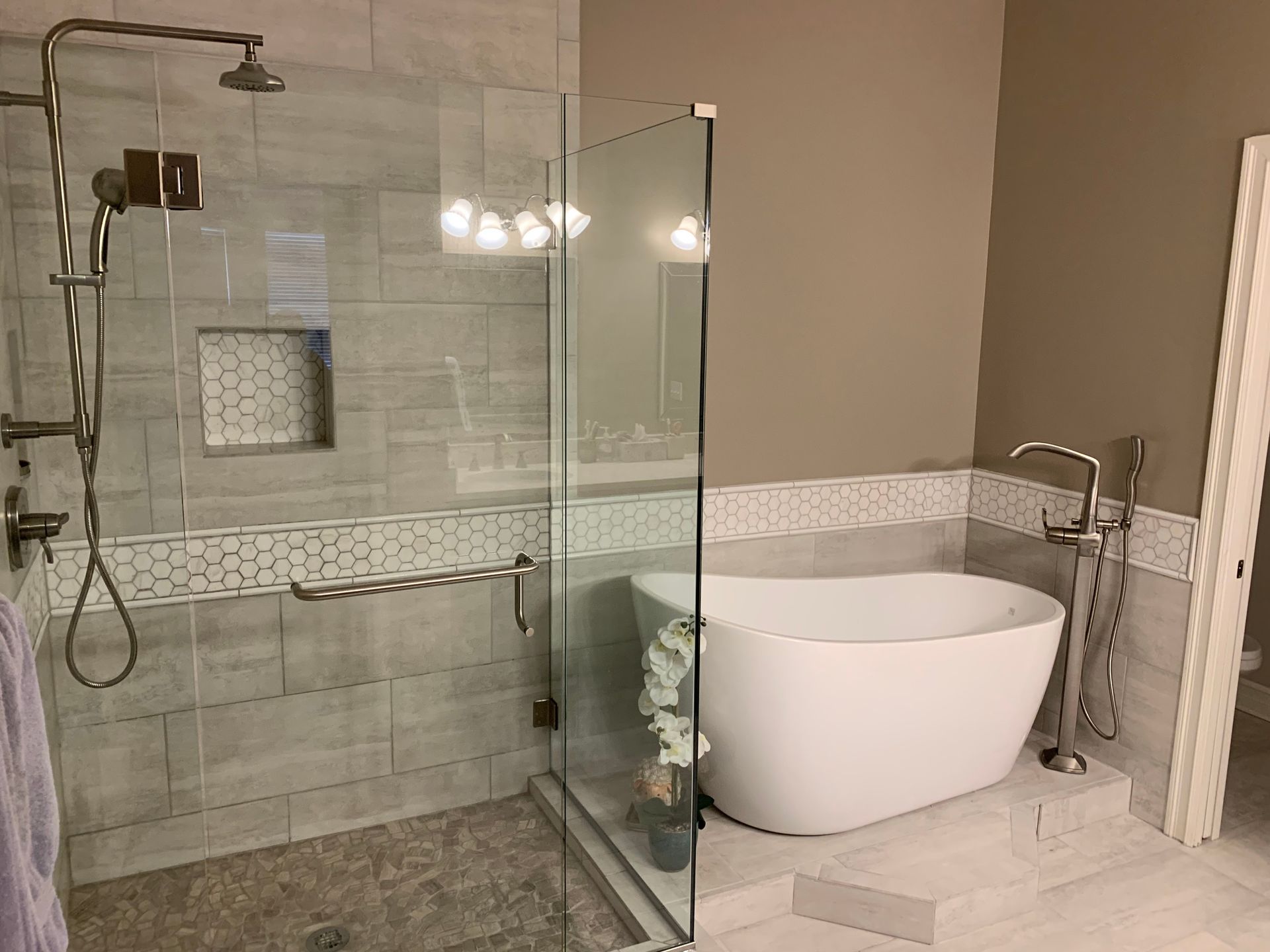 Modern bathroom with glass shower, freestanding white tub, and beige tile walls
