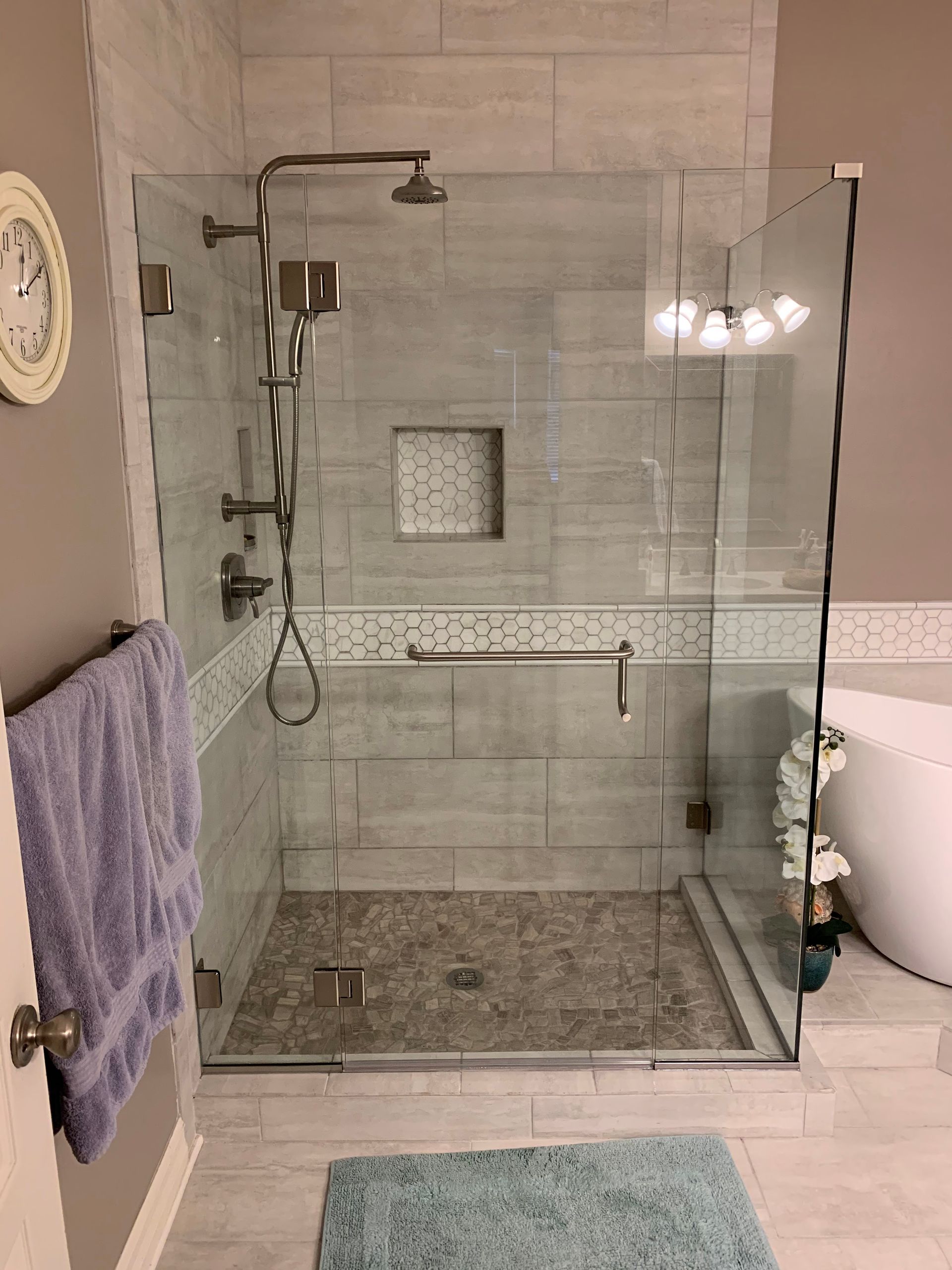 Glass walk-in shower with rainfall head, tiled walls, and a small bench in a bathroom