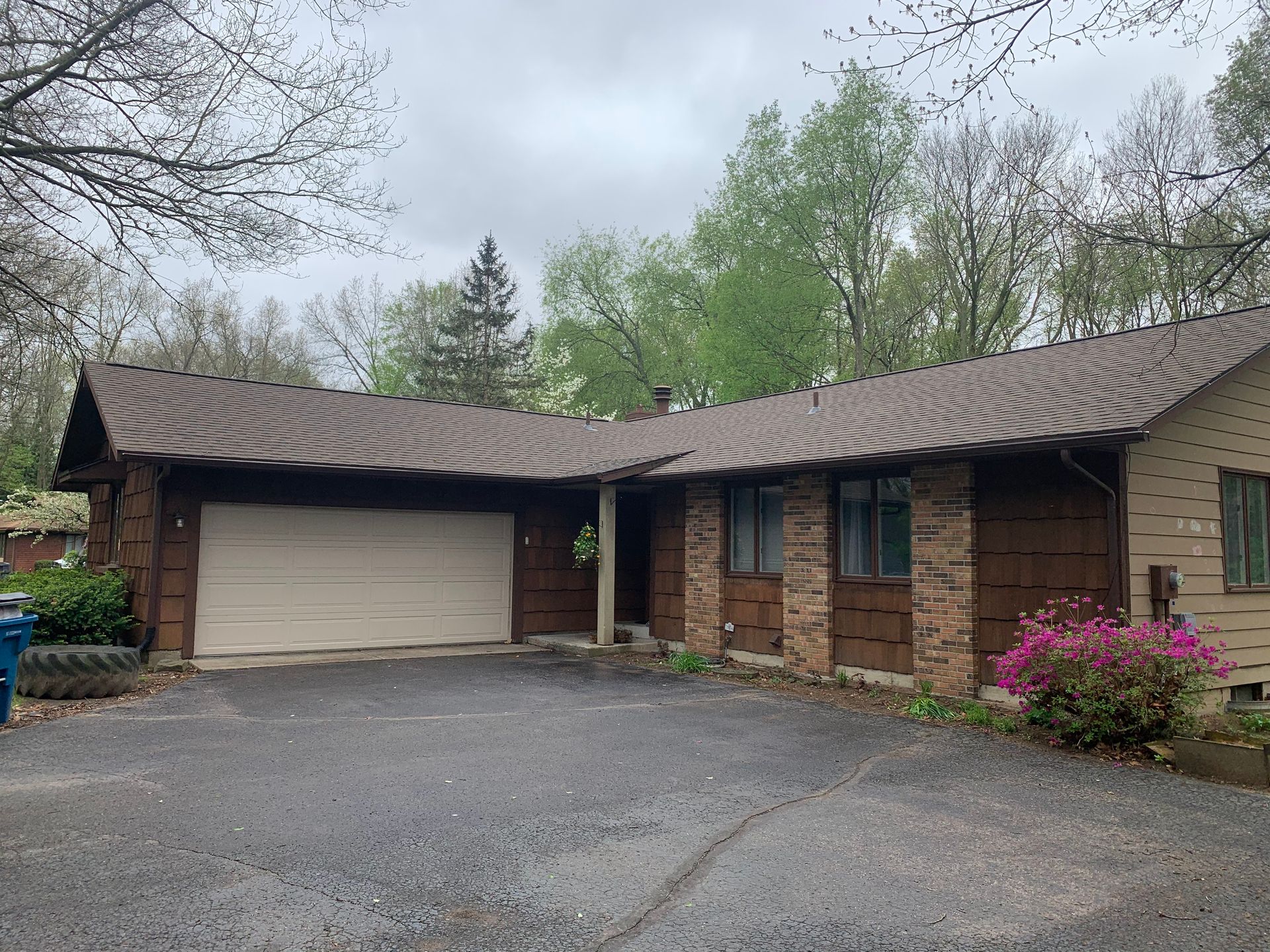 Suburban house with attached garage, brown roof, and pink flowering bush by the driveway