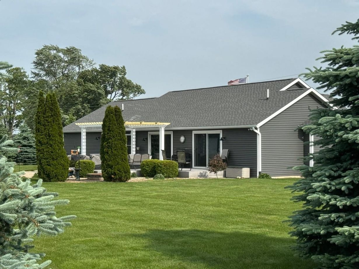 Single-story gray house with a manicured green lawn and tall evergreens