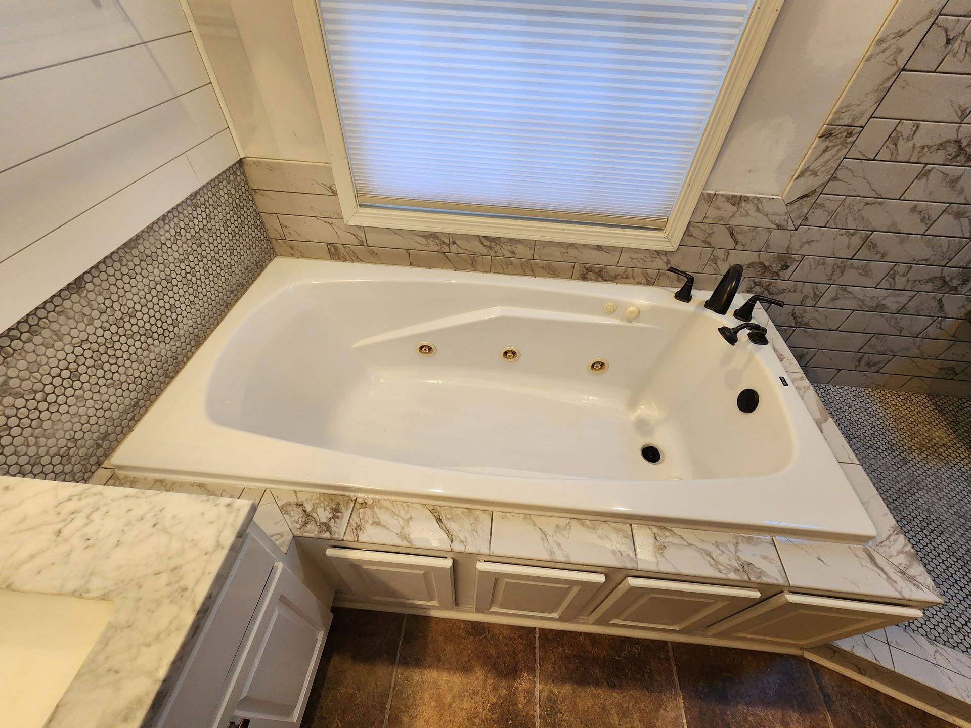 Corner soaking tub with marble surround, chrome fixtures, and frosted window in a tiled bathroom