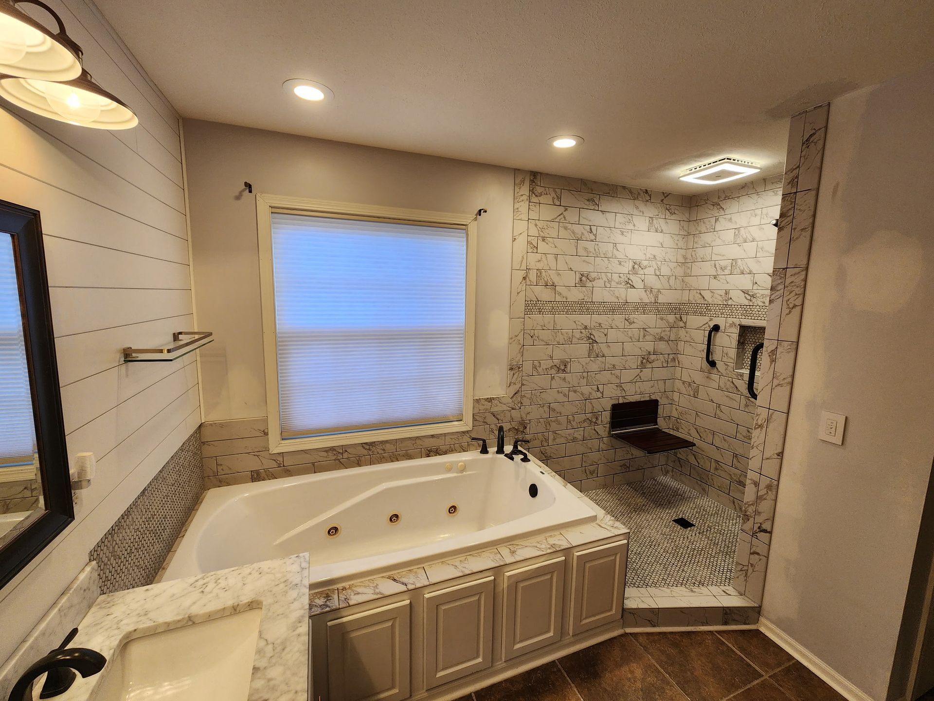 Bathroom with white soaking tub, tiled shower, and window with blinds under recessed lights