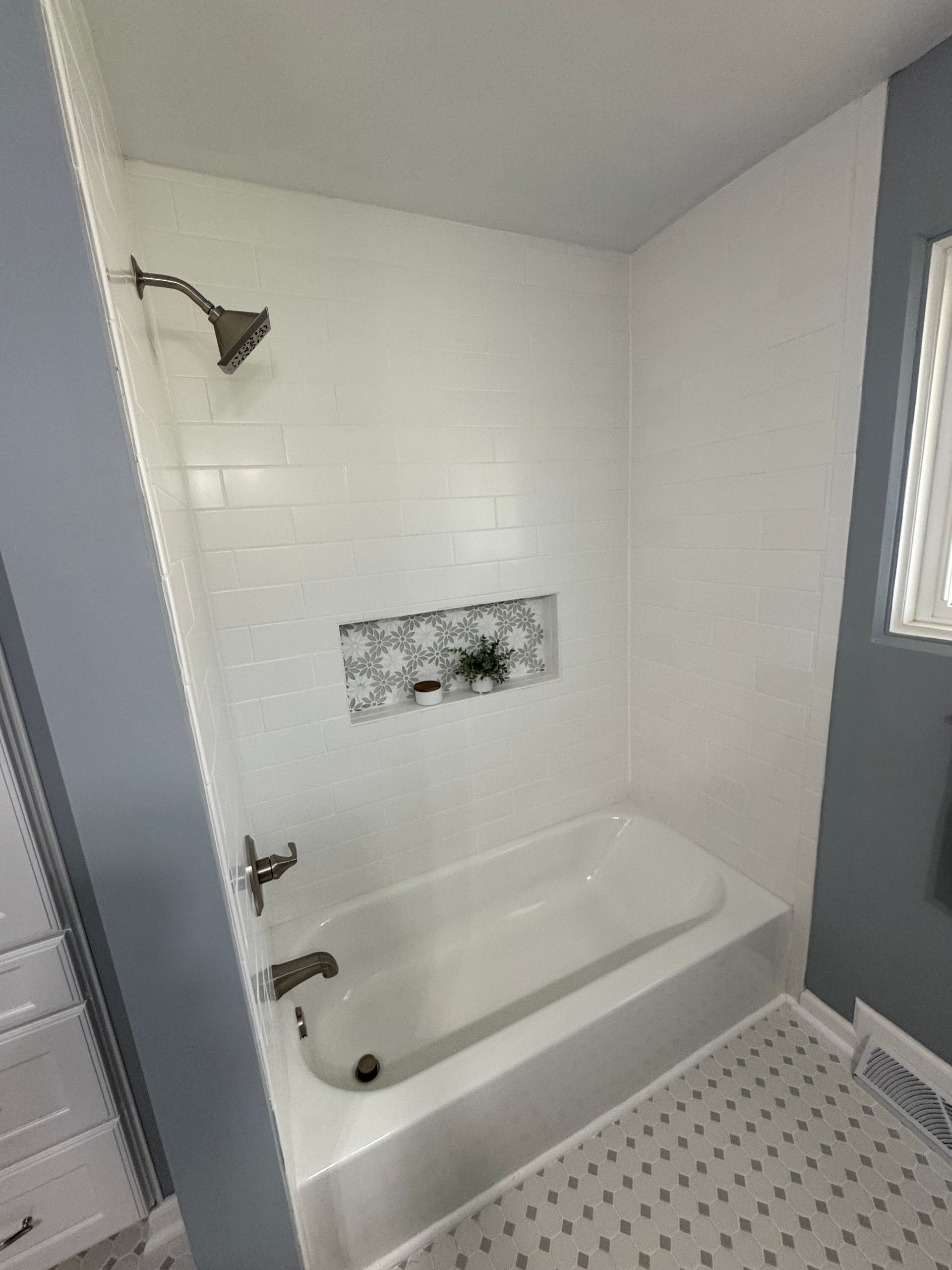 Empty white-and-gray bathtub and shower alcove with tiled floor and window.