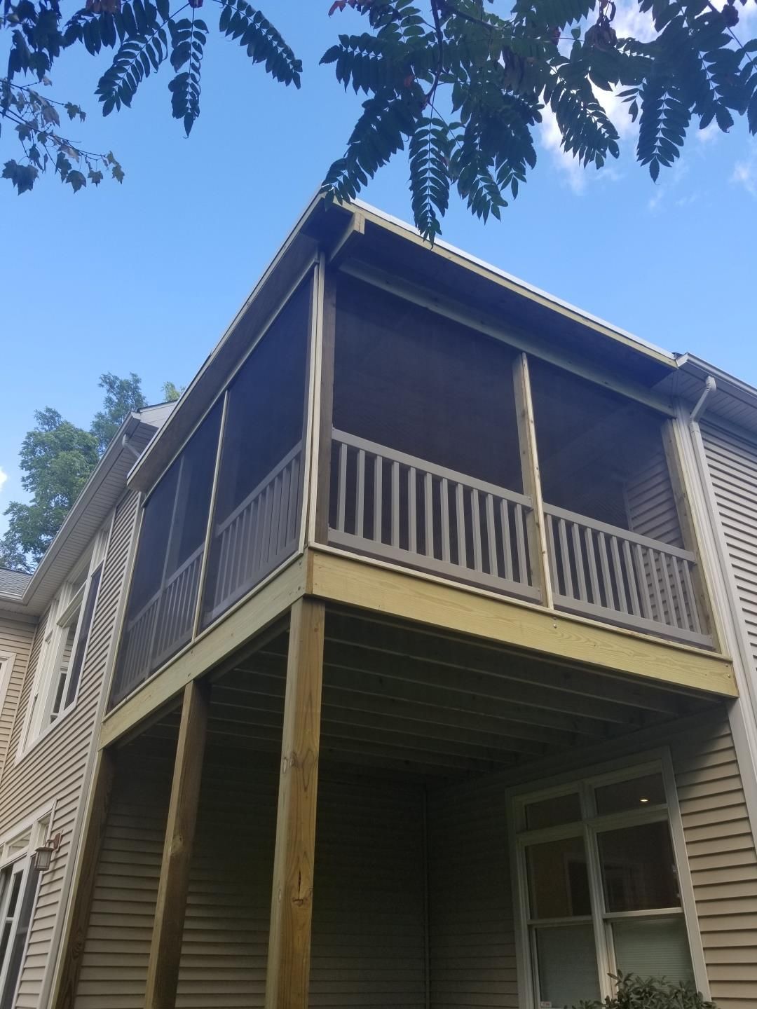 Wooden house with a covered porch and railing, viewed from below against a blue sky.