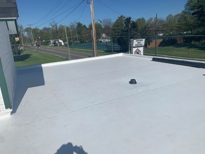 White flat rooftop with a vent under a clear blue sky near a roadside and trees