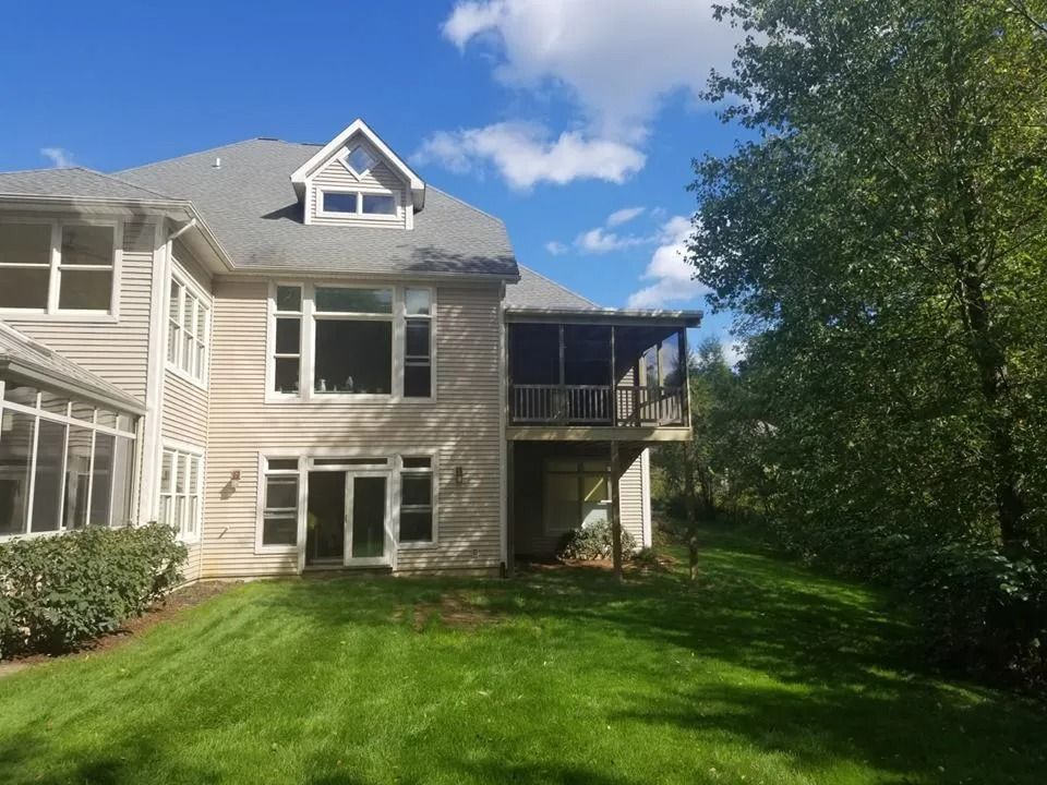 Backyard view of a two-story house with a green lawn, screened porch, and trees under a blue sky