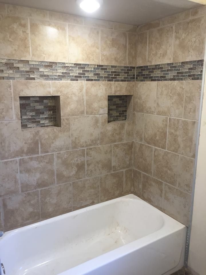 Tiled bathroom alcove with a white bathtub and two recessed wall niches above it.