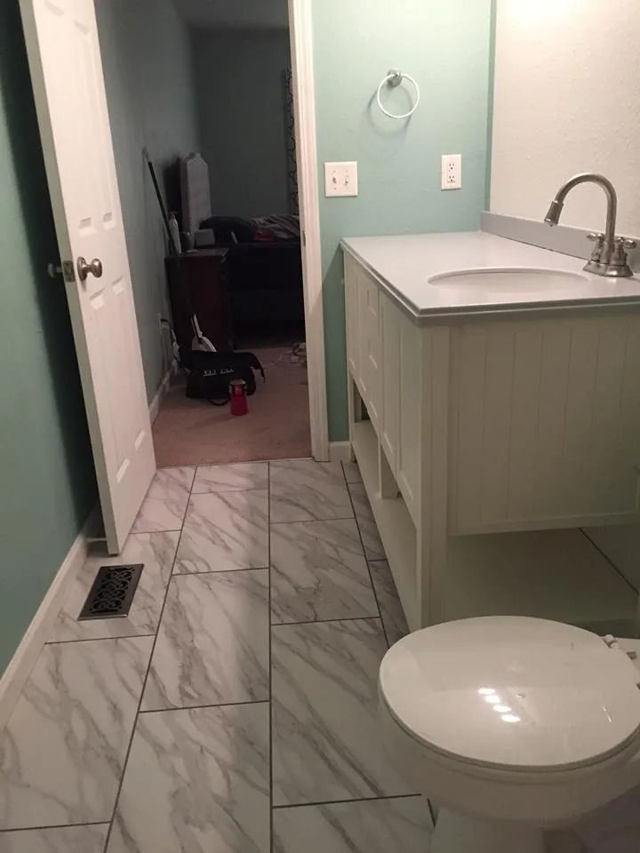 Small bathroom with marble tile, vanity sink, toilet, and open doorway to a dark room.