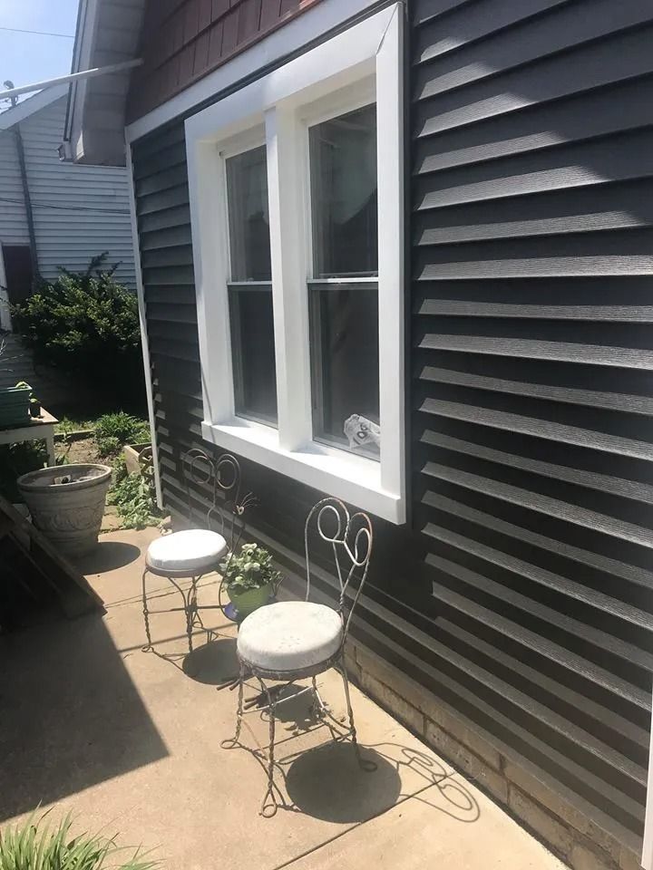 Narrow side yard with black siding, white-trimmed window, and two white stools on a concrete path