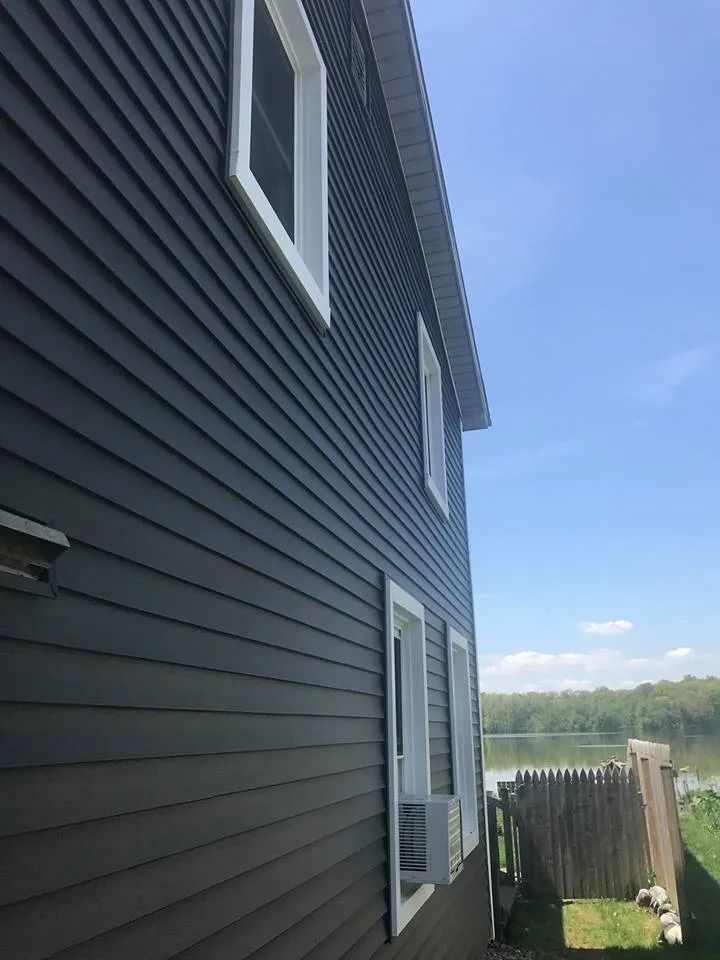 Gray-sided house with white windows beside a fenced yard overlooking water and sky