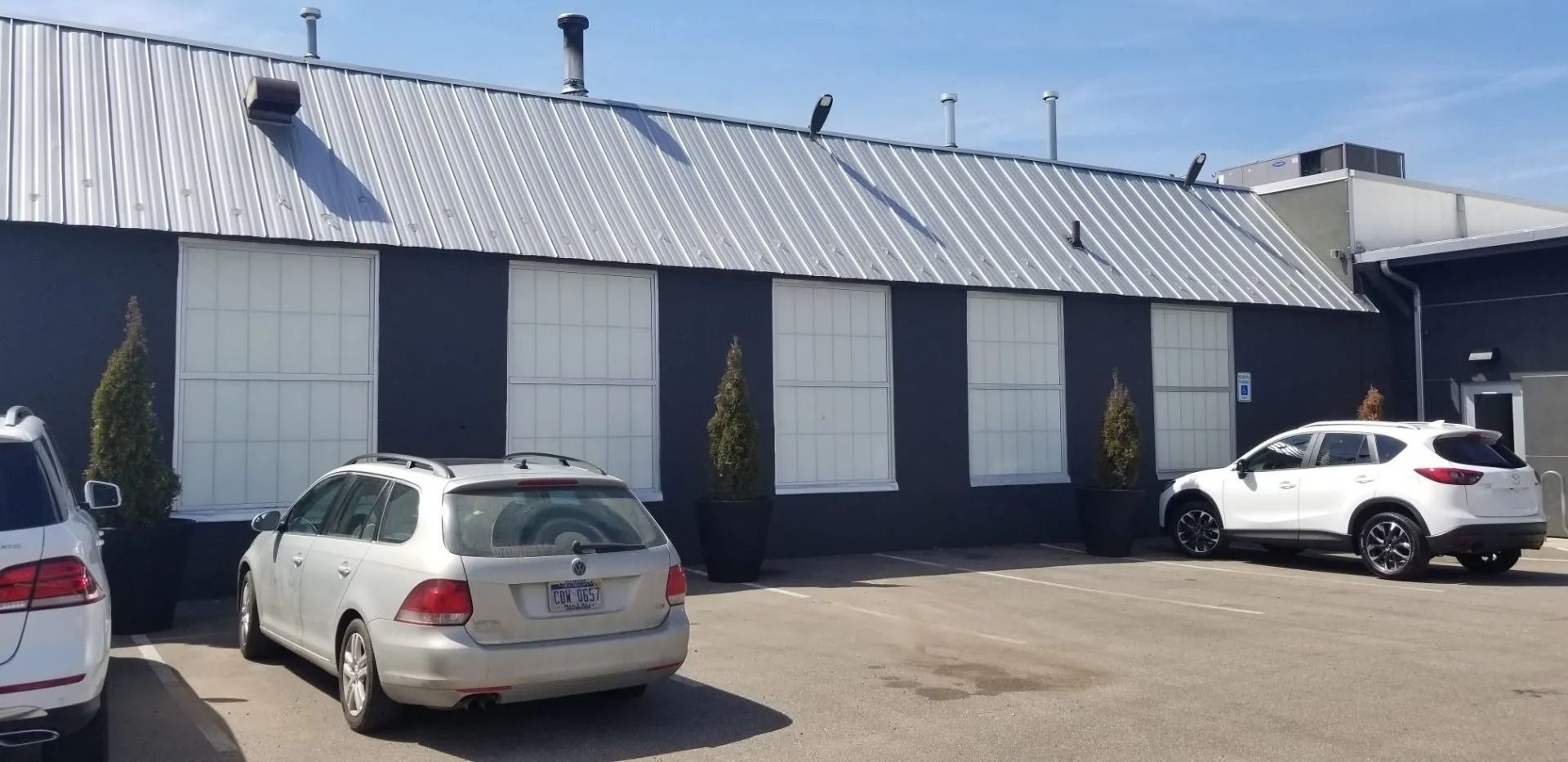 White industrial building with a metal roof and parked cars in front under sunny daylight