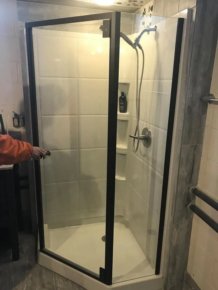 Corner shower enclosure with black frame and white tiled walls, showerhead and controls on the right.