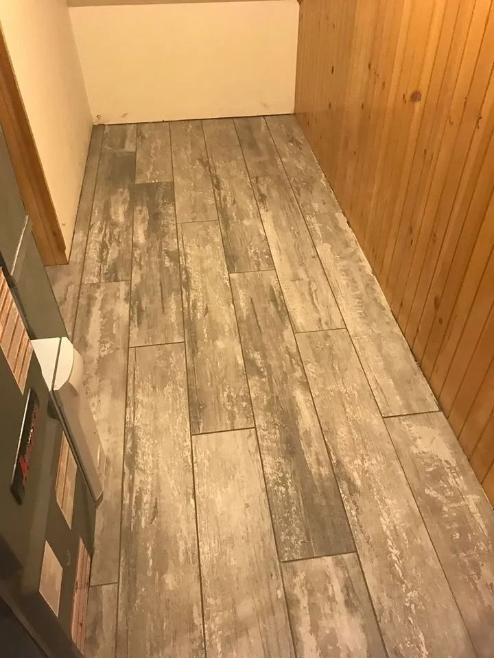 Narrow hallway with gray wood-look flooring, wood-paneled wall, and a beige wall at the end.