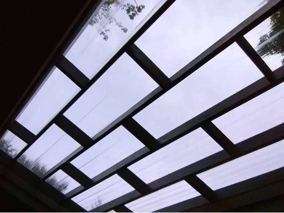 Diagonal glass skylight panes framing a pale sky and tree branches above
