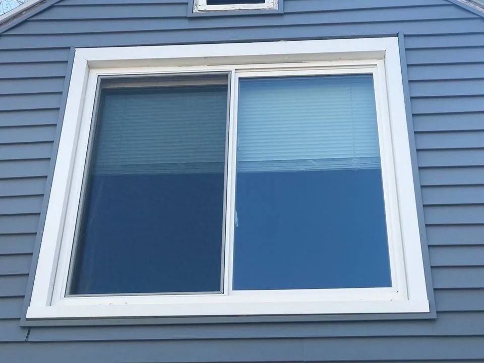 Blue house exterior with a white-framed double window and closed blinds