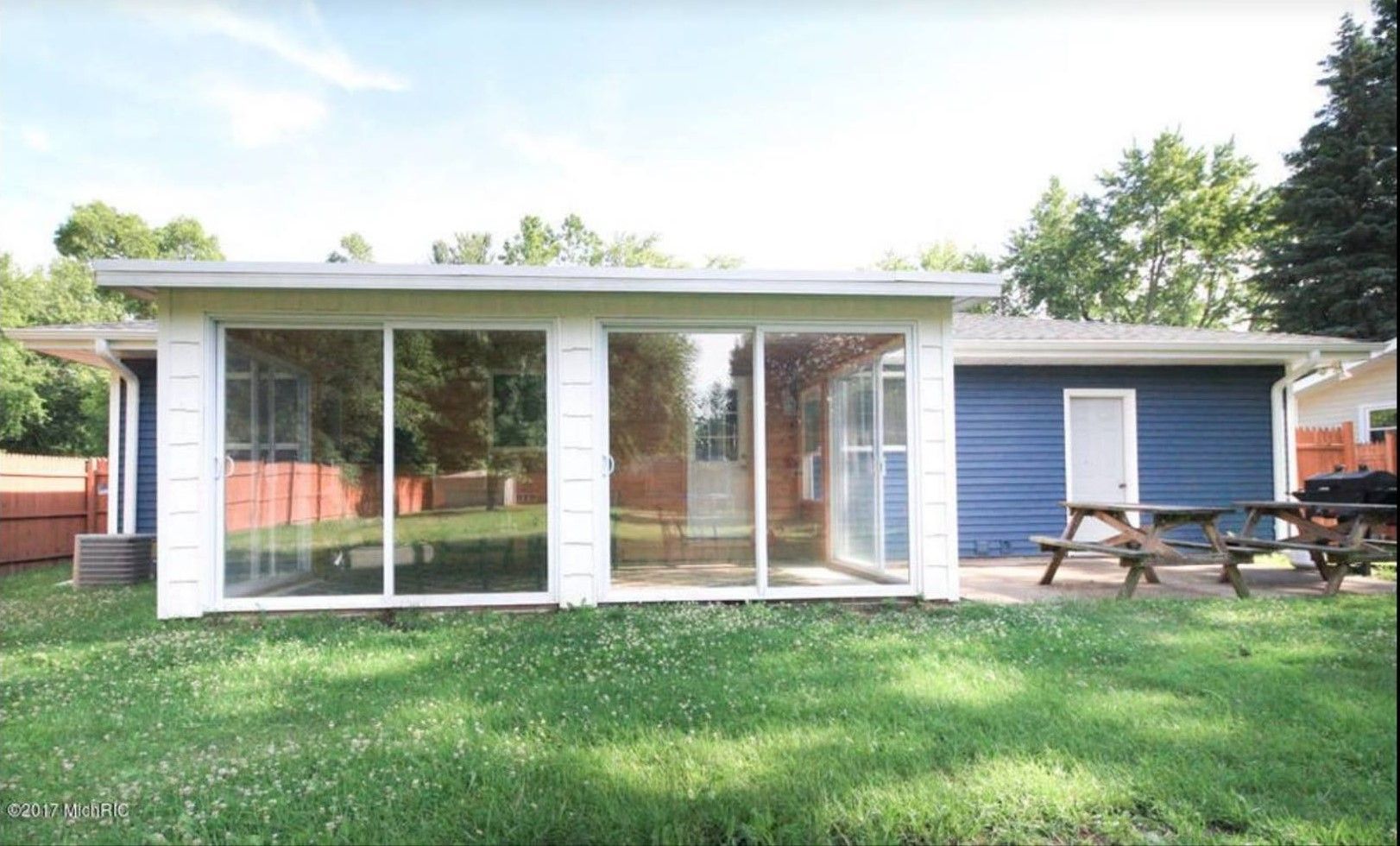 Modern single-story house with large front windows, blue siding, and a picnic table on the lawn.