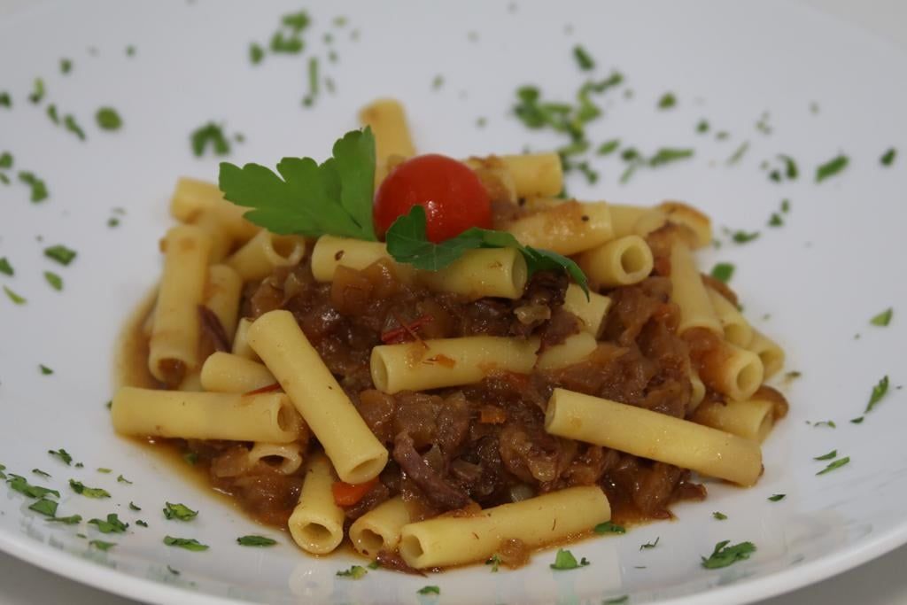 Un piatto bianco con sopra pasta e un pomodoro su un tavolo.