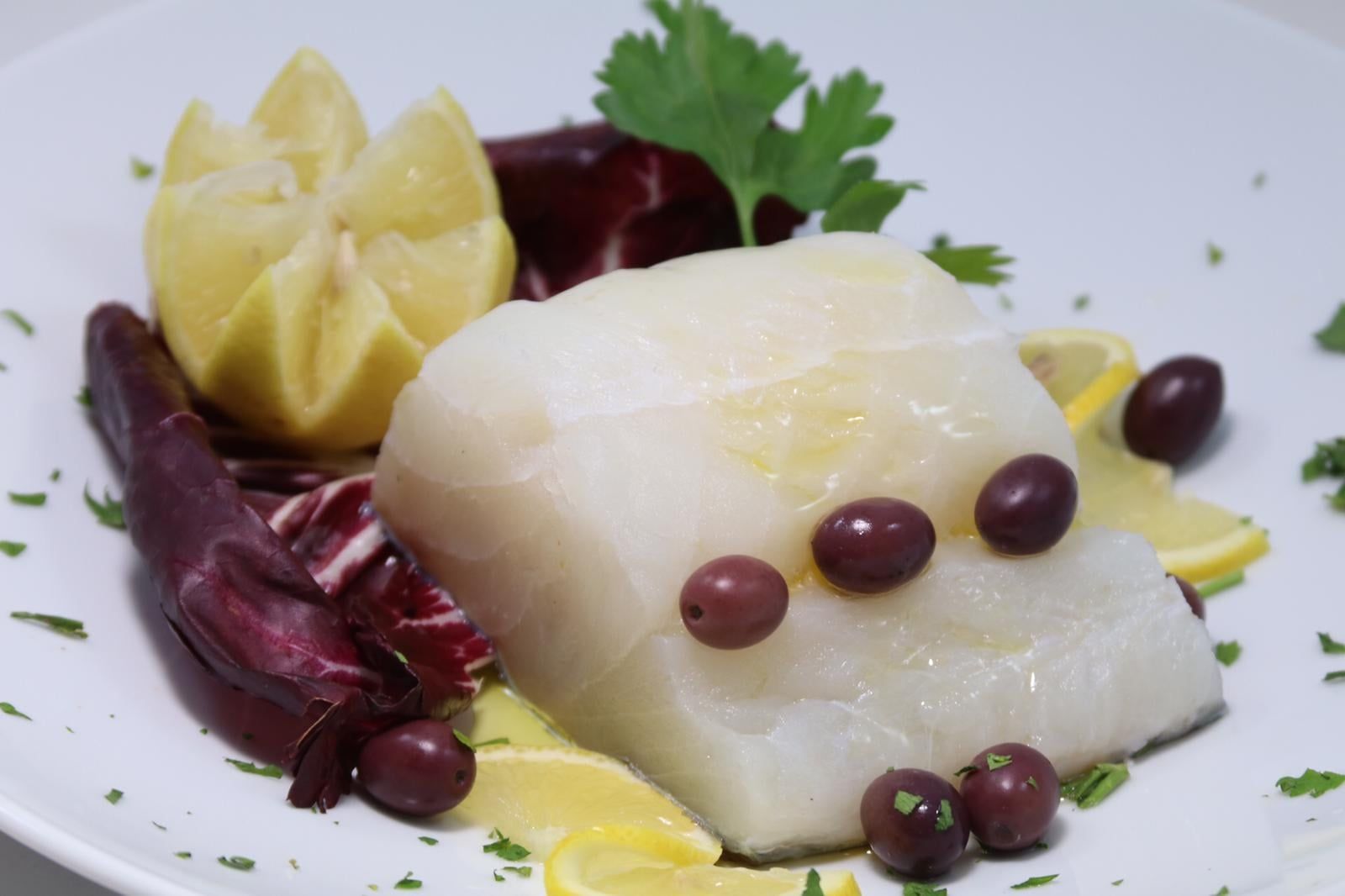 Un piatto bianco sormontato da un pezzo di pesce e olive