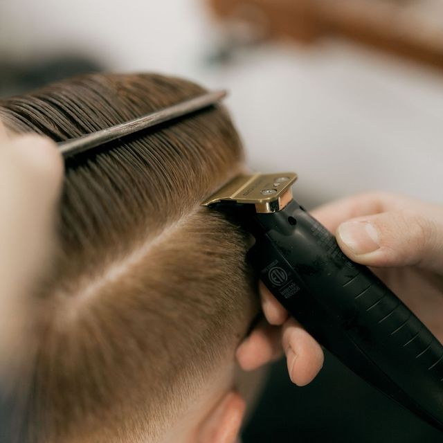 Hairdresser trimming a client’s hair with clippers and comb, close-up view