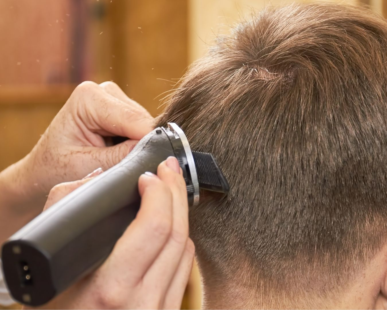 Clippers trimming the back of a person's short brown hair at a barbershop