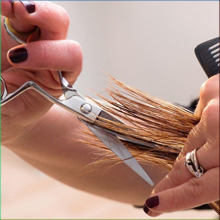 Hands cutting brown hair with silver scissors and comb, close-up in a salon.