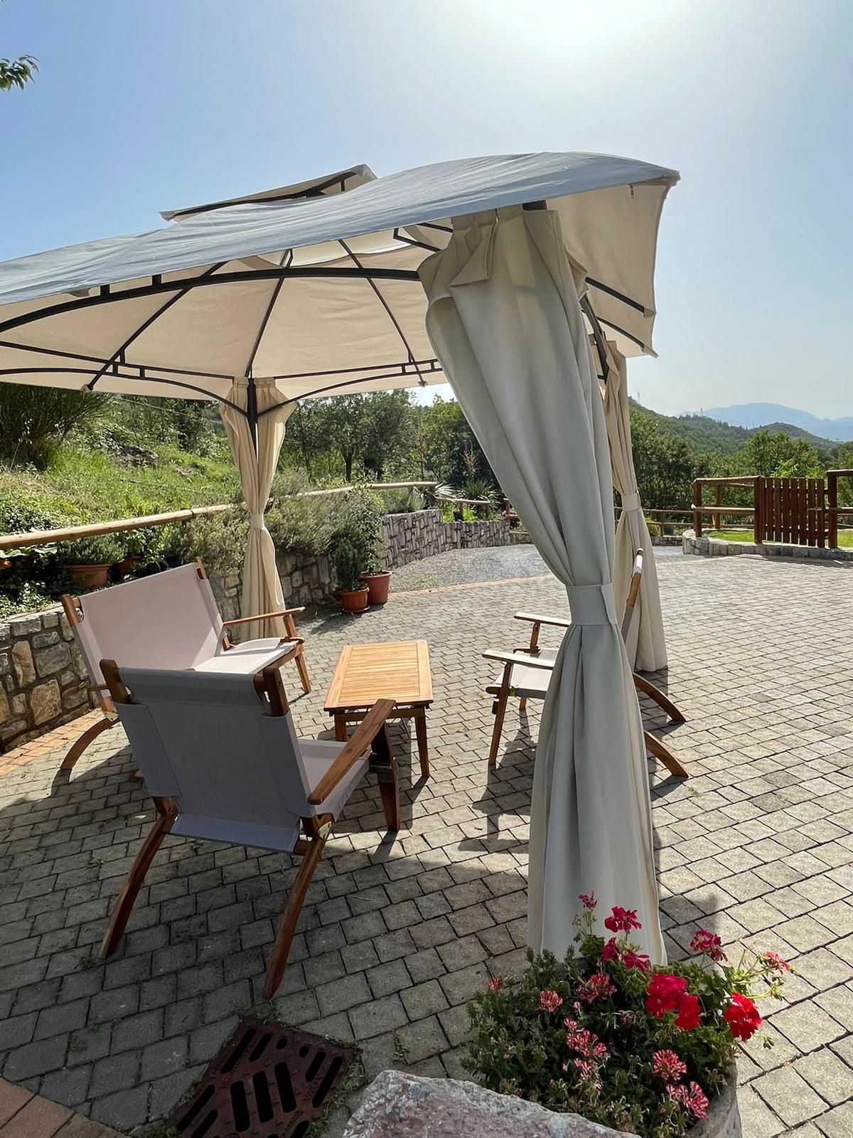 Sedie da giardino sotto un gazebo beige su una terrazza soleggiata con le montagne sullo sfondo.